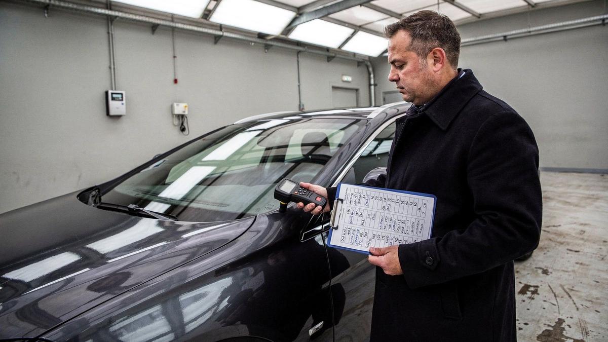 Consultant recording paint depth readings panel by panel on a dark luxury sedan.